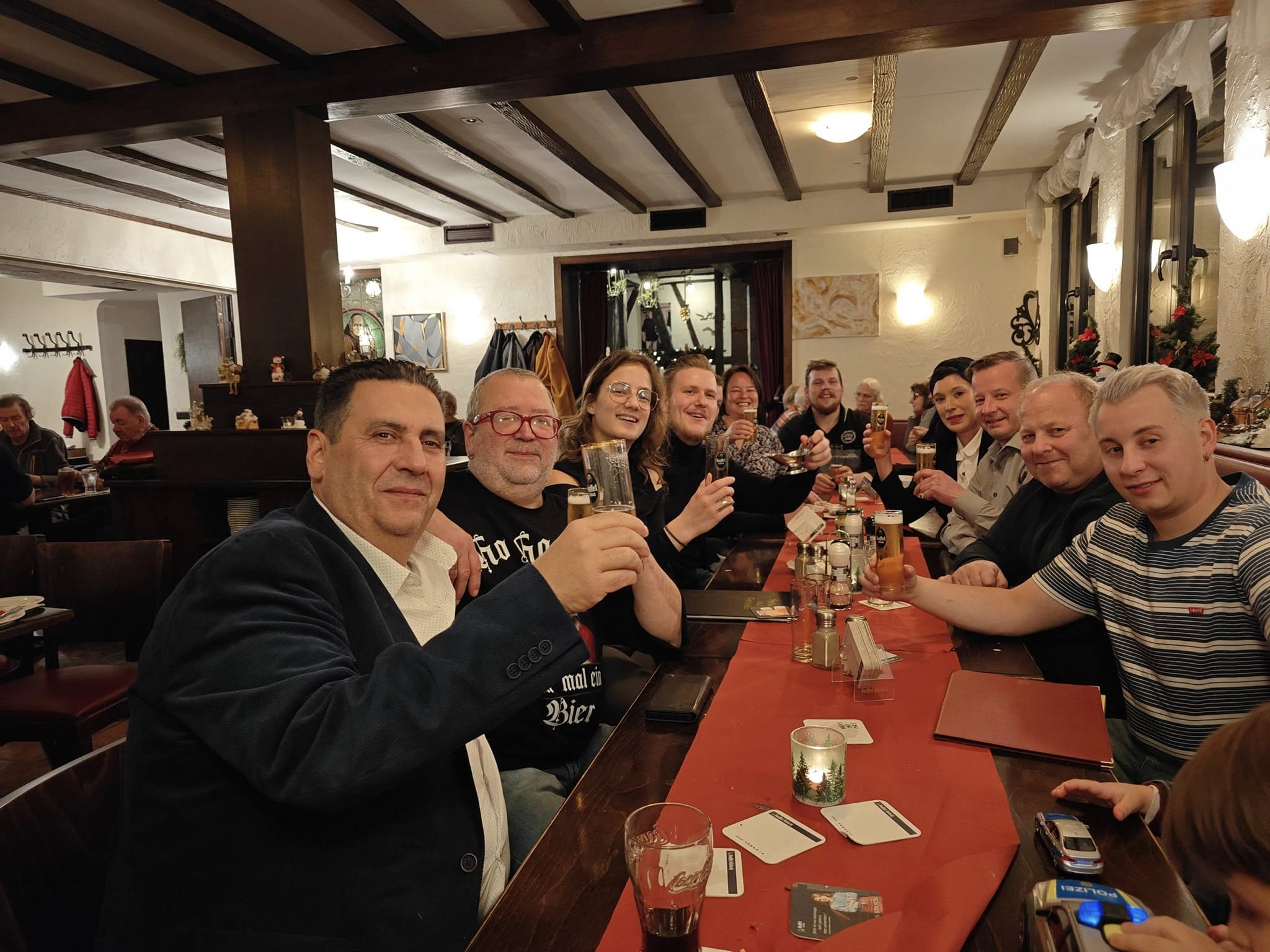 Miguel sitzt links mit Stammgästen an einem langen Tisch im Café Bistro Picasso.