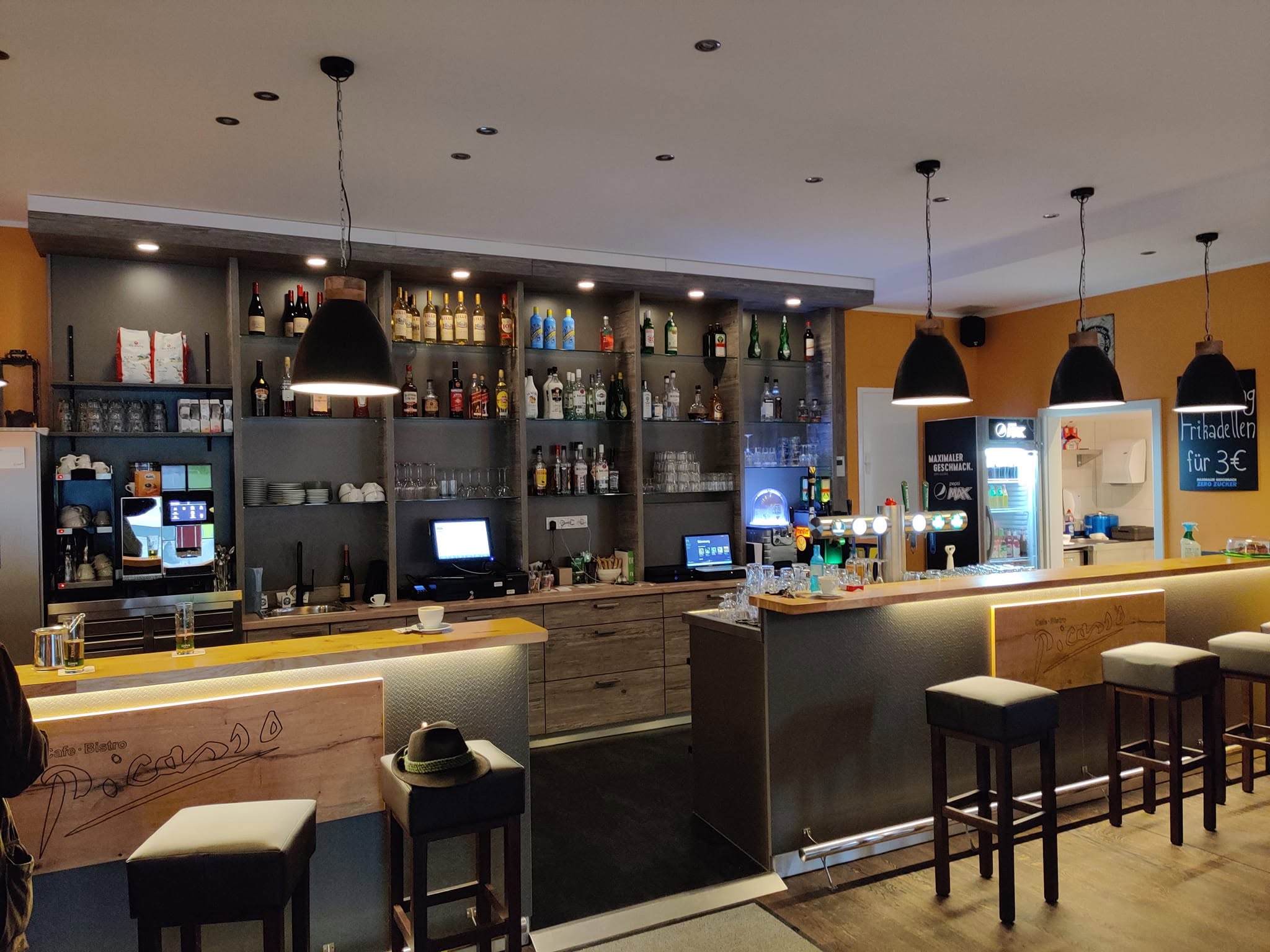 Warmer Innenraum der Picasso-Bar mit Theke, Sitzplätzen und beleuchteten Flaschenregalen.