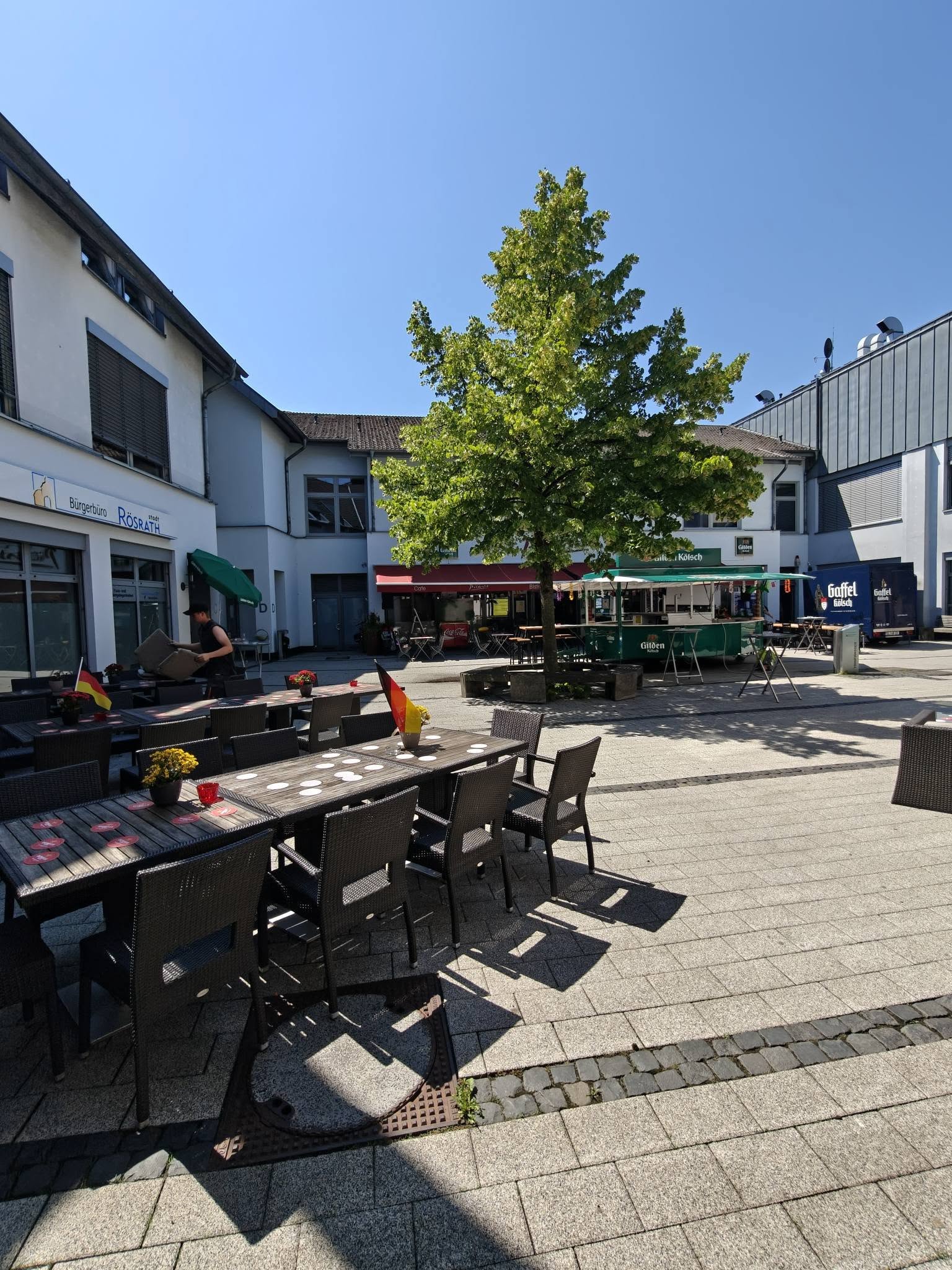 Sonnige Picasso-Terrasse mit Tischen, Deutschlandfähnchen und einem Gilden-Kölsch-Stand.