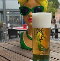Veltins-Bierglas vor einer dekorativen Figur auf der Picasso-Terrasse.